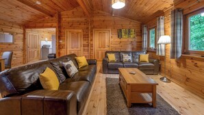 Ein Holzblockhaus-Interieur mit einer Couch, Sesseln, einem Couchtisch und einem Esstisch.