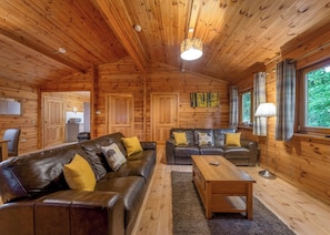A log cabin interior with a sofa, armchairs, a coffee table, and a dining table.