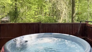 Ein Whirlpool auf einer Holzterrasse mit Wald im Hintergrund.