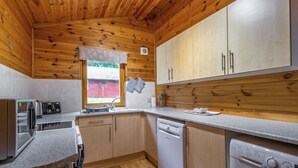 Eine kleine Küche mit Holzausstattung, einem Geschirrspüler, einer Waschmaschine und einem Fenster mit Blick auf ein rotes Gebäude.
