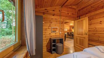 Ein Holzblockhaus-Innenraum mit einem Bett, einem kleinen Tisch, einem Mülleimer und einer Tür zu einem Essbereich.