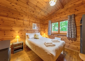 Une chambre à coucher dans une cabane en bois, avec un lit, des lampes de chevet, une fenêtre avec des rideaux et une vue sur les arbres.