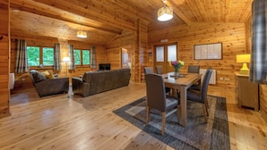 A wooden cabin interior with a sofa, dining table, chairs, and a television. - Woodland Birch Lodge (Ellesmere)