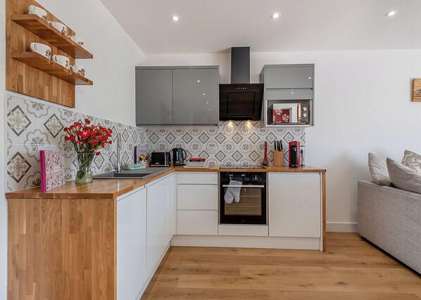 A compact kitchen with white cabinets, a built-in oven, a coffee machine, and a wooden shelf above the counter. - 2 bedroom accommodation in Orby (Orby)