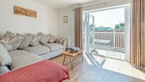 Un soggiorno con un divano grigio, una coperta rossa, un tavolino con una scatola e vista su un giardino tramite una porta in vetro.