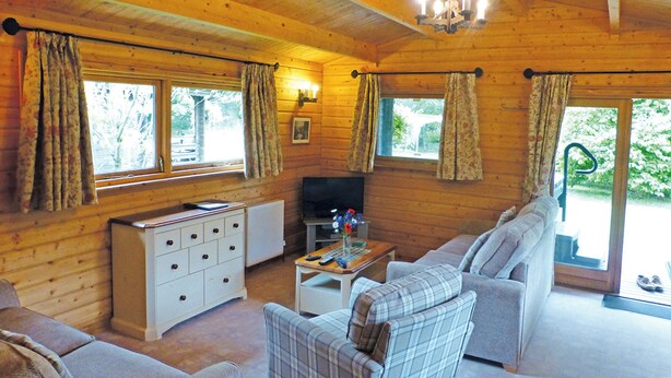 A wooden cabin interior with a sofa, television, and a small table. - Timber lodge with one queen size double and one twin. (Kentisbeare, Nr Cullompton)