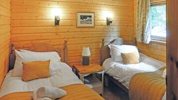Une chambre de style cabane avec deux lits, une table de chevet avec une lampe, un tableau encadré au mur et une fenêtre avec des rideaux.
