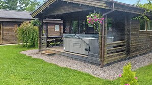 A wooden cabin with a patio, a hot tub, and a small deck. - Timber lodge with one queen size double and one twin. (Kentisbeare, Nr Cullompton)
