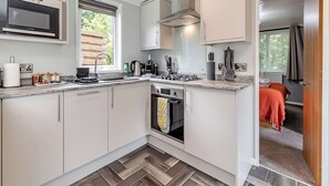A compact kitchen with a microwave, stove, sink, and oven. - Buxton Lodge with hot tub (Longnor, Nr. Buxton)