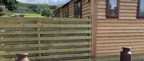 A wooden cabin with a sloped roof, a wooden fence, and two metal containers.