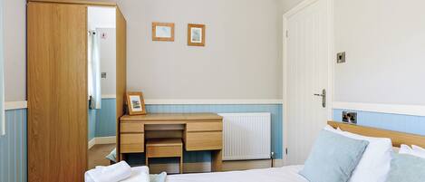 Une chambre d’hôtel avec un lit, un bureau en bois, un radiateur et une porte.