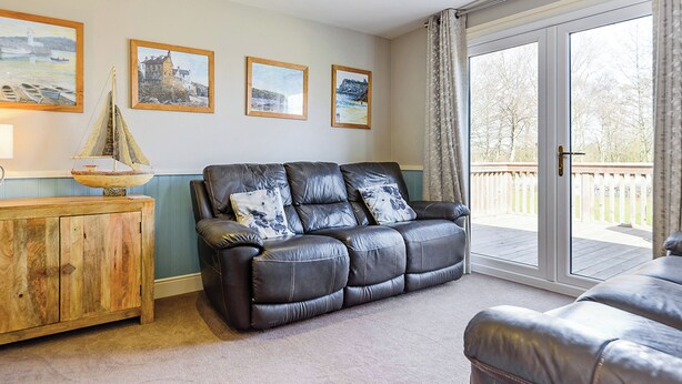 A living room with a leather sofa, wooden cabinet, and a view of the outdoors through a glass door. - 3 bedroom accommodation in Pickering (Pickering)