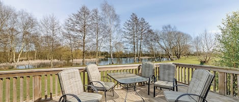 A deck with outdoor furniture, a view of a lake, and trees in the background.