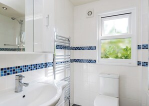 A bathroom with a white sink, a toilet, a shower, and a window with a plant view.