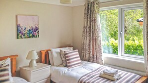 Un dormitorio con dos camas, una mesita de noche con lámpara, una ventana con cortinas y un cuadro en la pared.