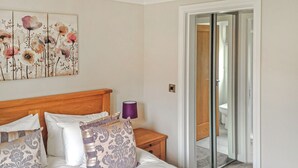 Un dormitorio con cama, almohadas, una mesita de noche, una lámpara y una puerta que da a un baño.