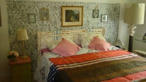 Un dormitorio con cama, mesita de noche, lámpara y una pared decorada con marcos.