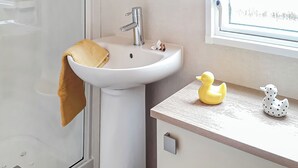 Een badkamer met een witte wastafel, een handdoek, een zeepdispenser in de vorm van een eend en een raam met uitzicht.