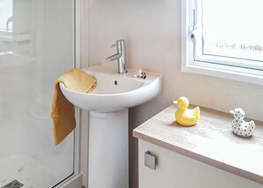 Een badkamer met een witte wastafel, een handdoek, een zeepdispenser in de vorm van een eend en een raam met uitzicht.
