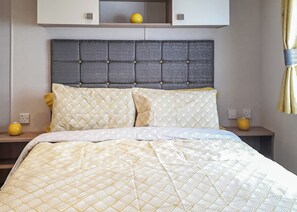 Een bed met een beddekleed met patroon, een grijs gestoffeerd hoofdbord en twee nachtkastjes met gele vazen.