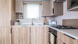 A modern kitchen with wooden cabinetry, a gas stove, a sink, and a window with blinds.