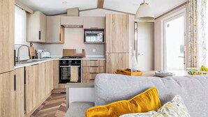 A compact kitchen with a microwave, stove, and sink, a sofa with cushions, and a large window.
