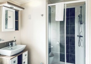 A bathroom with a white sink, a mirror, a glass shower enclosure, and a towel hanging on the shower door.