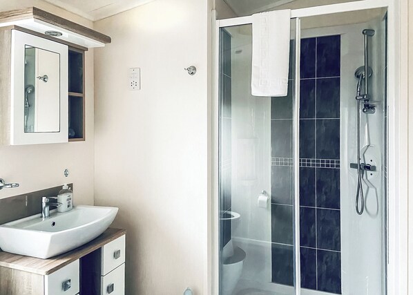 A bathroom with a white sink, a mirror, a glass shower enclosure, and a towel hanging on the shower door.