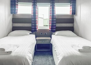 A twin room with two beds, a small bedside table, and a window with curtains.