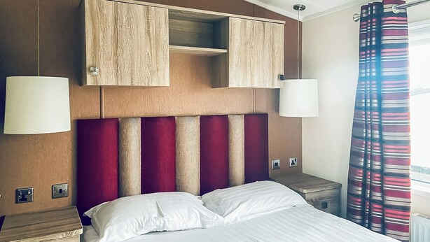 Une chambre d’hôtel avec un lit, une tête de lit en bois, deux lampes de chevet, une table de chevet et une fenêtre avec des rideaux.