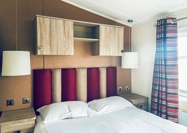 A hotel room with a bed, a wooden headboard, two bedside lamps, a nightstand, and a window with curtains.