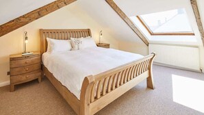 Un dormitorio con techo inclinado, estructura de cama de madera, ropa de cama blanca, dos mesitas de noche y un tragaluz.