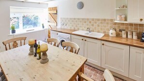 Una cocina con una mesa de madera, sillas, un lavamanos, una lavadora y una ventana con vistas a la vegetación.
