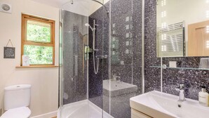Une salle de bain dotée d’une douche à parois de verre, de toilettes, d’un lavabo avec un miroir et d’une fenêtre donnant sur un espace verdoyant.