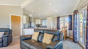 A modern living room with a black leather sofa, a wooden door, a kitchen in the background, and a dining area with a table and chairs. - 1 bedroom accommodation in Shrewsbury (Shrewsbury)