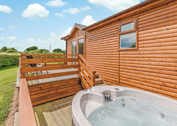 A wooden cabin with a hot tub, wooden deck, and a view of the sky.