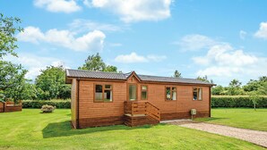 A wooden cabin with a porch, a small staircase, and a gravel path leading to the entrance. - Luxury lodge with king-size bed with en suite shower. (Shrewsbury)