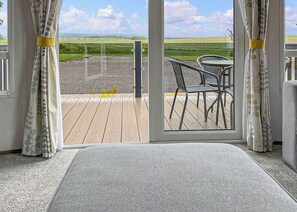 Habitación con vista a una terraza de madera y sillas exteriores, puerta corrediza de vidrio y piso alfombrado.