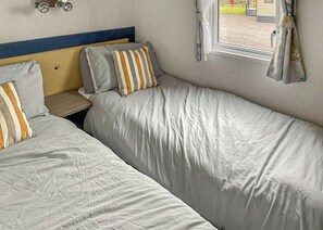 Un dormitorio con dos camas, cabecero de madera, ventana con cortinas e iluminación empotrada en la pared.