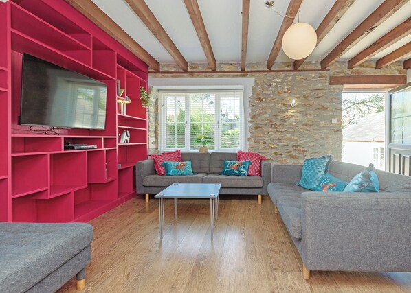 Ein Wohnzimmer mit rotem Bücherregal, grauem Sofa, Couchtisch und Fernseher.