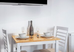 Une table à manger avec une bouteille de champagne, deux verres et une corbeille dressée pour deux personnes.