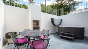 A patio with a round table and four chairs, a hot tub, and a grill.
