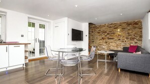 A modern living space with a dining area, a sofa, a stone wall, and a television.