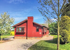 Une maison rouge à un étage, avec des fondations en briques, une cheminée et un petit porche à l’avant.