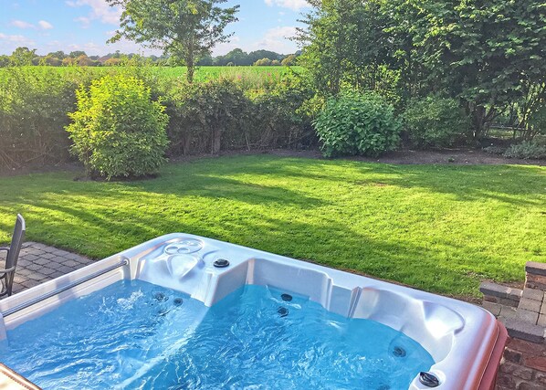 A hot tub in a backyard with a grassy lawn and trees.