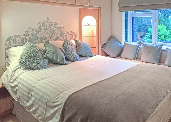 A bedroom with a bed, pillows, a nightstand, a lamp, and a window with a view of greenery. - 3 bedroom accommodation in Easingwold (Easingwold)
