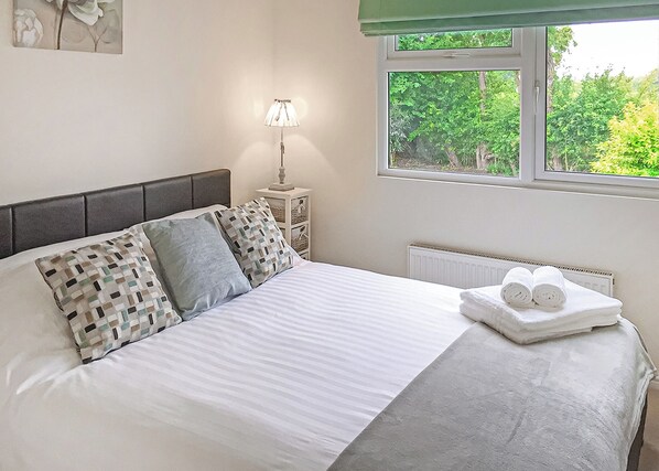 Un lit bien fait, avec des oreillers, une lampe de chevet, un radiateur et une fenêtre donnant sur un paysage verdoyant.