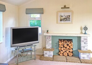 A living room with a flat-screen TV on a glass stand, a fireplace with stacked logs, and a framed picture above it. - 1 bedroom accommodation in Easingwold (Easingwold)