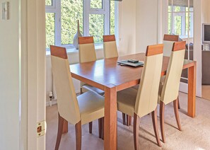 A dining area with a wooden table and six chairs, a vase on the windowsill, and a television in the background.