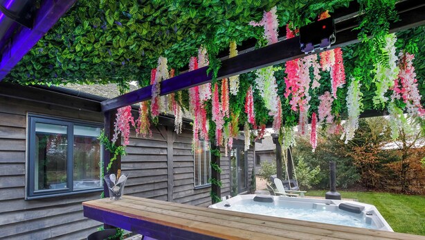 A hot tub with a wooden deck, a pergola with hanging flowers, and a wooden house in the background. - 1 bedroom accommodation in South Duffield, Nr York (South Duffield, Nr York)